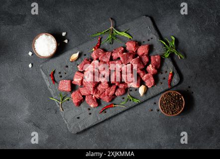 Diced cubed beef meat on stone board with thyme and peppers Stock Photo