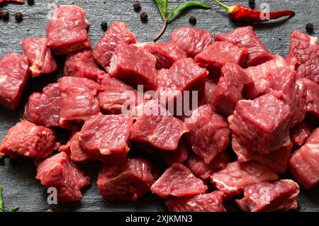 Diced cubed beef meat on stone board with thyme and peppers Stock Photo
