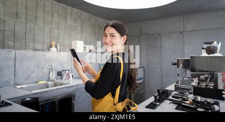 Smiling Barista in Modern Industrial Coffee Shop Using Digital Tablet for Orders Stock Photo