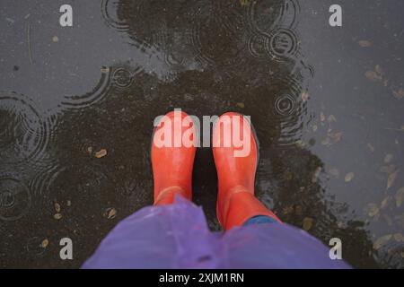 Woman wearing red rubber boots standing in rippled puddle, top view Stock Photo