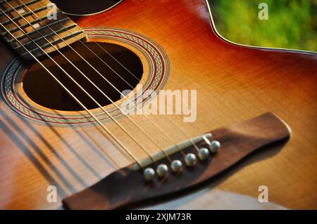 Acoustic guitar. Close-up image of old acoustic guitar in a garden: shiny brown deck instrument with metal and nylon strings over fretboard. Stock Photo