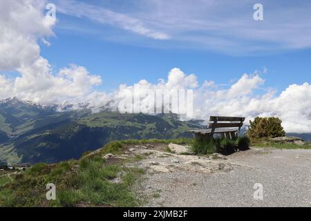View of a wooden bench in the high mountains with fantastic views of mountain ranges and the cloudy blue sky Stock Photo