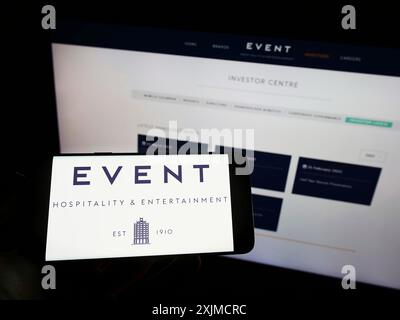 Stuttgart, Germany, 05-22-2022: Person holding cellphone with logo of company Event Hospitality Entertainment Ltd. on screen in front of business Stock Photo