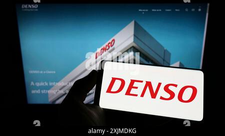 Stuttgart, Germany, 06-04-2022: Person holding smartphone with logo of Japanese automotive company DENSO Corporation on screen in front of website. Stock Photo