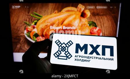 Stuttgart, Germany, 06-18-2022: Person holding cellphone with logo of Ukrainian company Myronivsky Hliboproduct (MHP) on screen in front of webpage. Stock Photo