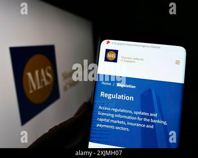 Stuttgart, Germany, 07-16-2022: Person holding smartphone with webpage of Monetary Authority of Singapore (MAS) on screen in front of logo. Focus on Stock Photo
