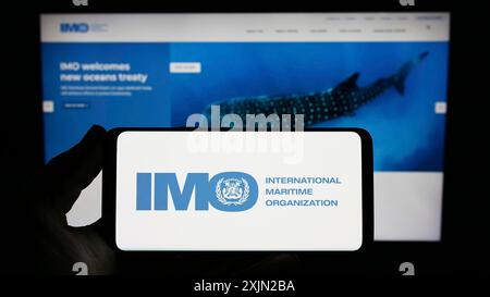 Stuttgart, Germany, 03-07-2023: Person holding smartphone with logo of International Maritime Organization (IMO) on screen in front of website. Focus Stock Photo