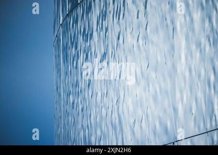 Shiny metallic wall made of rippled steel plates reflects blue sky, contemporary architecture background photo Stock Photo