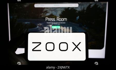 Stuttgart, Germany, 03-19-2023: Person holding smartphone with logo of US autonomous vehicle company Zoox Inc. on screen in front of website. Focus Stock Photo