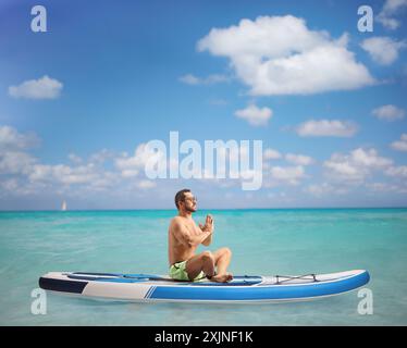 Full length profile shot of a man practicing meditation on a SUP in the sea Stock Photo