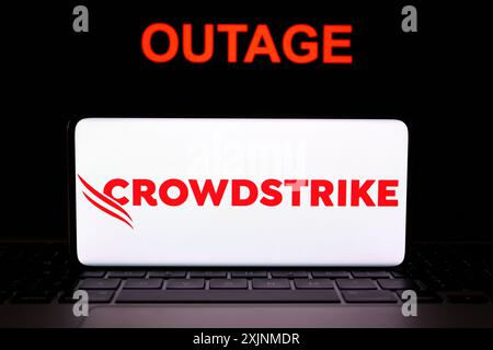CrowdStrike logo seen on screen of smartphone and the word OUTAGE seen behind it. Cybersecurity company behind the global IT outage. Concept. Stafford Stock Photo