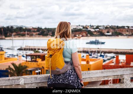 Woman tourist with backpack exploring Portimao city during vacation in Algarve, Portugal. Solo travel Stock Photo
