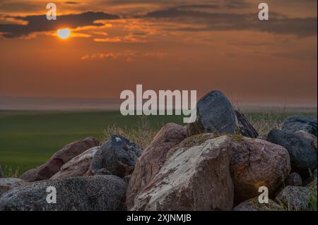 Sun setting behind a pile of field stones on the prairie at the Great Sandhills, Saskatchewan, Canada Stock Photo