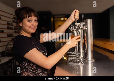 Portrait of waitress in profile filling a glass of beer from the tap. Stock Photo