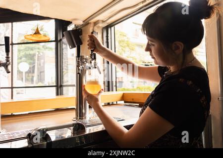 Profile silhouette of a woman serving draft beer in a bar with large windows during the day. Stock Photo