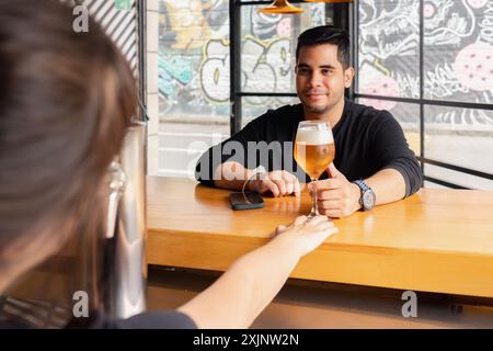 A man smiles as he receives a freshly poured beer from a bartender at the bar of a contemporary bar. Stock Photo