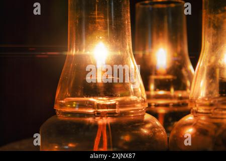 three glass paraffin kerosene lamp lit on a table, orange glow, flame glitter Stock Photo