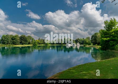 Lake landscape with white floating cottages and blue sky with large white clouds reflecting on the water and with large green trees on the shoreline Stock Photo