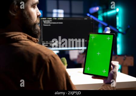 Admin doing software debugging using isolated screen tablet, checking errors in lines of code displayed on PC monitors. Man working from home fixing coding issues using chroma key portable device Stock Photo