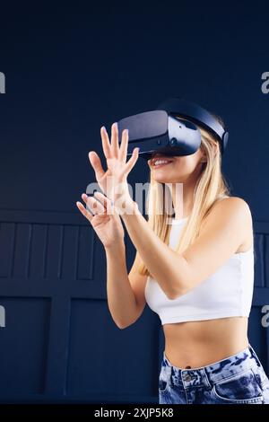 A woman wearing a virtual reality headset interacts with a virtual world, her hands outstretched as if reaching for something. Stock Photo