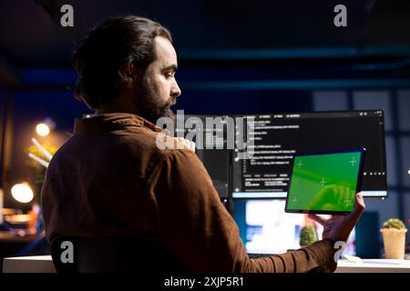 Programmer using green screen tablet to fix vulnerabilities in software. Man taking care of security exposures in operating system, writing code on mockup portable device Stock Photo