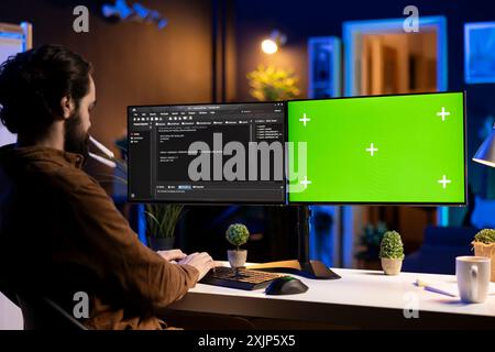 Freelancing admin using green screen computer monitors to filter malicious traffic from cybercriminals attempting to corrupt company data. IT expert in apartment working on mockup desktop PC Stock Photo
