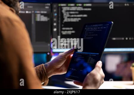 Computer scientist doing software quality assurance using tablet, reading source code before implementing it. Developer inspecting coding on portable device, looking to fix potential issues Stock Photo