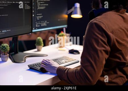 System administrator doing software debugging on PC at home, checking broken lines of code displayed on monitors. IT professional in living room fixing coding problems, typing on keyboard Stock Photo