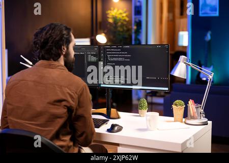 Computer operator doing software debugging on PC at home, checking broken lines of code displayed on monitors. IT expert in apartment fixing coding problems, typing on keyboard Stock Photo