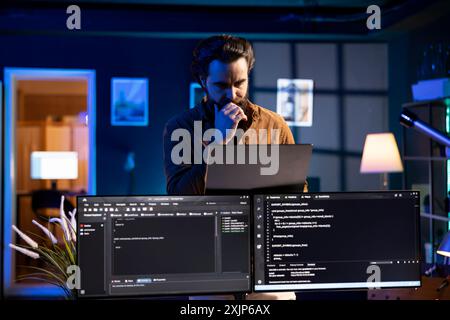 Man working from home developing software in Java programming language using laptop. Programmer walking through apartment thinking how to solve coding problems using notebook Stock Photo