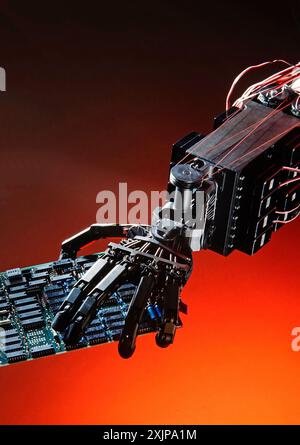 A robotic hand, with multiple joints and wires, holds a green circuit board in front of a red background. The hand is made of black metal and is in a Stock Photo