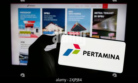 Stuttgart, Germany, 06-30-2023: Person holding cellphone with logo of Indonesian company PT Pertamina (Persero) on screen in front of business Stock Photo