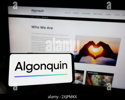 Stuttgart, Germany, 07-28-2023: Person holding smartphone with logo of Canadian company Algonquin Power Utilities Corp. on screen in front of Stock Photo