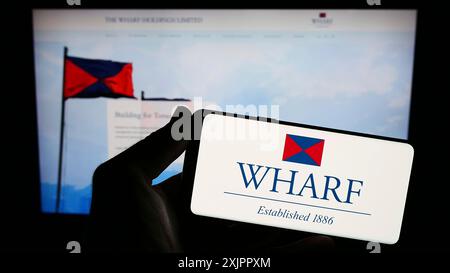 Stuttgart, Germany, 08-17-2023: Person holding smartphone with logo of Chinese company The Wharf Holdings Limited on screen in front of website. Stock Photo