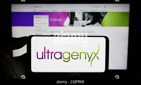 Stuttgart, Germany, 08-26-2023: Person holding cellphone with logo of US company Ultragenyx Pharmaceutical Inc. on screen in front of business Stock Photo