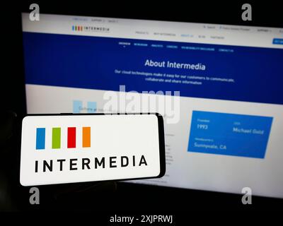 Stuttgart, Germany, 08-28-2023: Person holding smartphone with logo of US company Intermedia Cloud Communications on screen in front of website. Stock Photo