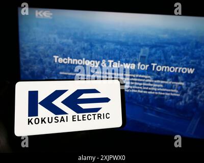 Stuttgart, Germany, 09-24-2023: Person holding cellphone with logo of Japanese company Kokusai Electric Corporation on screen in front of webpage. Stock Photo