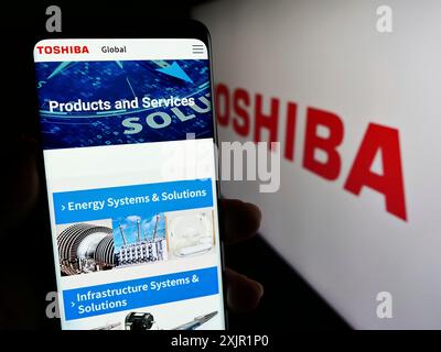 Stuttgart, Germany, 11-23-2023: Person holding smartphone with web page of Japanese electronics company Toshiba Corporation in front of logo. Focus Stock Photo