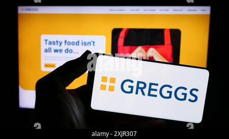 Stuttgart, Germany, 12-14-2023: Person holding smartphone with logo of British bakery chain company Greggs plc in front of website. Focus on phone Stock Photo