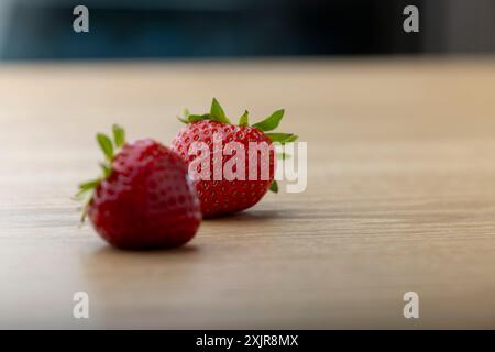 Two fresh strawberries rest on a wooden surface, with a soft-focus background adding depth to the composition. The strawberries' vibrant red color Stock Photo