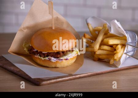 Delicious crispy chicken burger with fresh coleslaw and a soft brioche bun, served alongside golden french fries on a wooden tray. Stock Photo