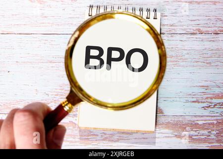 Business concept. Letters BPO. Business Process Outsourcing in a white notebook on old boards through a magnifying glass in a man's hand Stock Photo