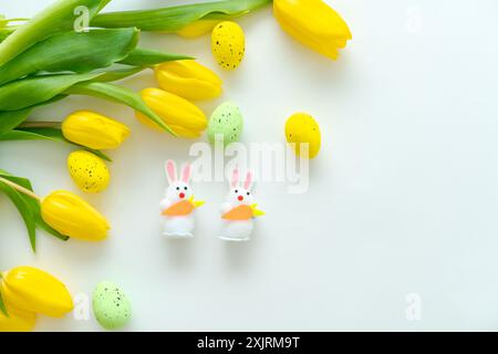 Easter decorations featuring yellow tulips, speckled eggs, and bunny figures on a white background. Concept of spring and celebration Stock Photo