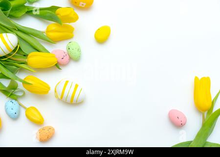 Yellow tulips and various colorful Easter eggs arranged on a white background. Easter celebration concept Stock Photo