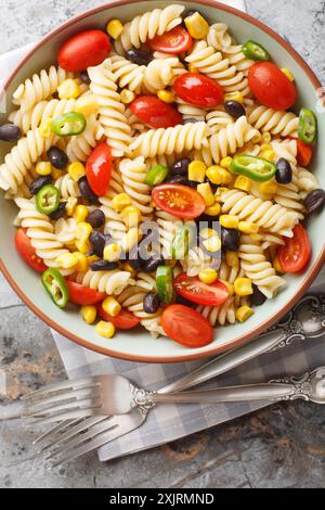 Bright mix pasta salad with black beans, tomato, jalapeno and corn close-up in a plate on the table. Vertical top view from above Stock Photo