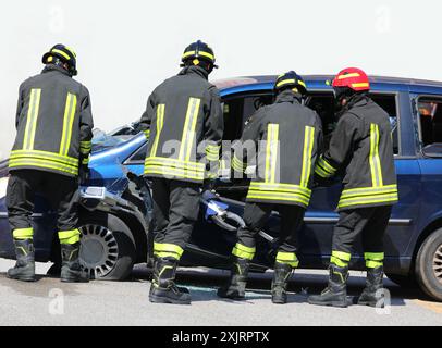 Firefighters using jaws of life to open car door after road accident Stock Photo