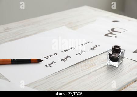 Calligraphy. Papers with written word Branch in Arabian language, inkwell and brush on white wooden table, closeup Stock Photo