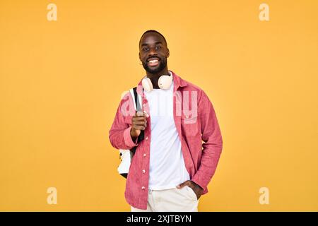 Happy young African man student standing isolated on yellow background. Stock Photo