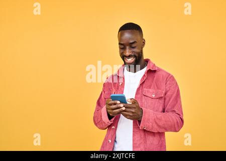 Young happy African man standing isolated on yellow background holding phone. Stock Photo