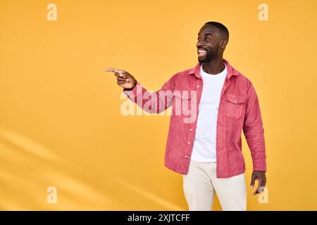 Happy young African American man isolated on yellow background pointing aside. Stock Photo